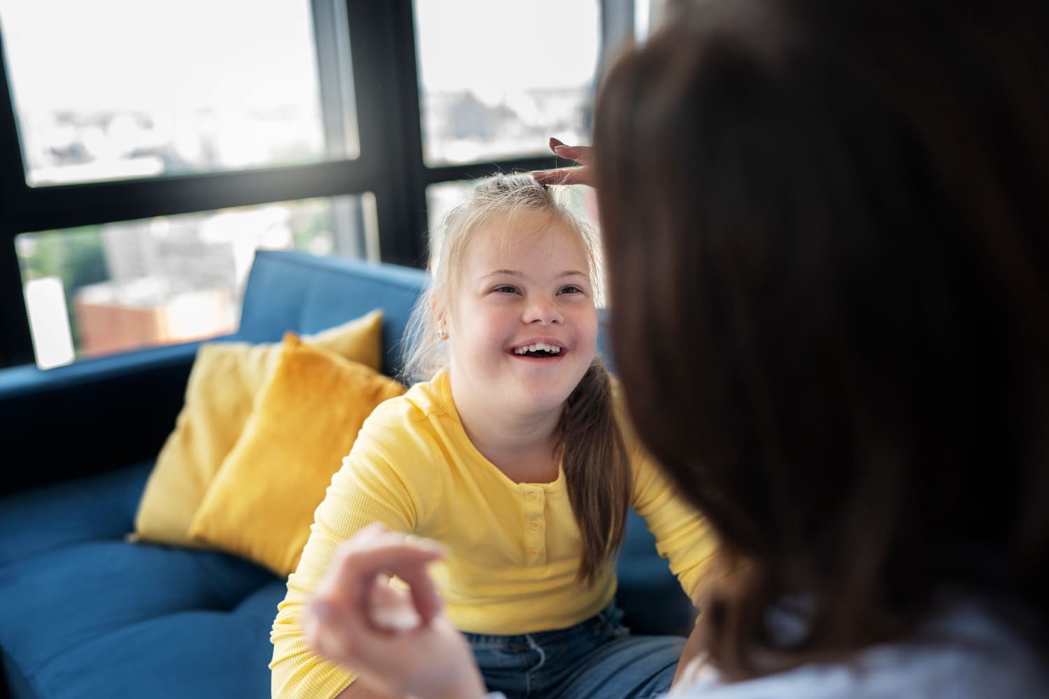 Menina com síndrome de Down sorrindo durante uma conversa com uma adulta, sentadas em um sofá