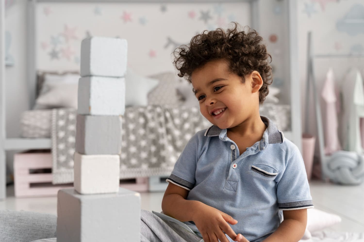 Menino pequeno sorrindo ao lado de uma torre de blocos de montar no quarto