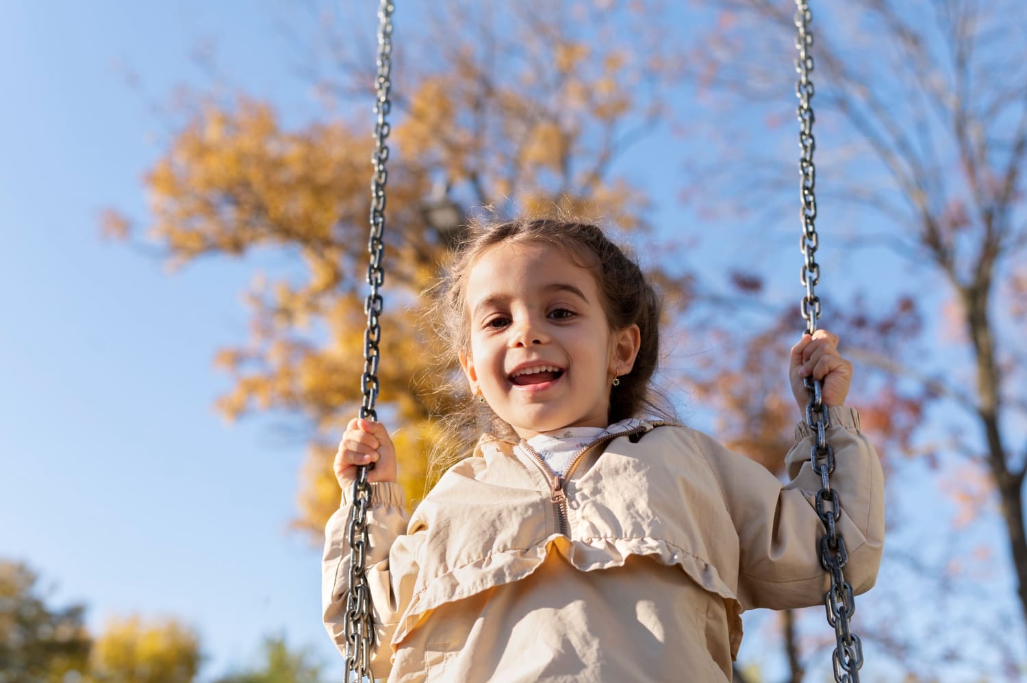 Menina sorrindo em um balanço de parque, vista de baixo com o céu ao fundo